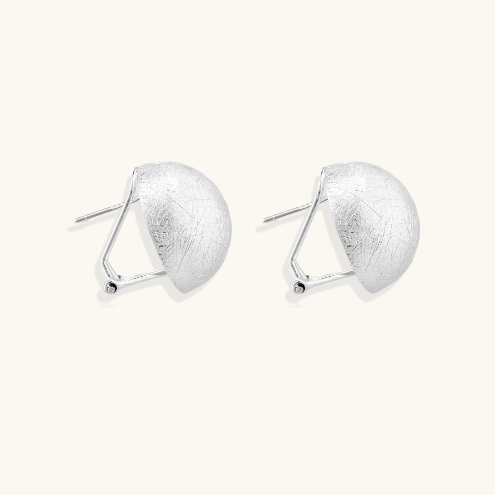 Brushed sterling silver half-dome clip-on earrings with textured surface against cream background