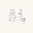 White gold plated sculptural hoop earrings with organic wavy edges and reflective metallic finish on cream background
