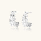 White gold plated sculptural hoop earrings with organic wavy edges and reflective metallic finish on cream background