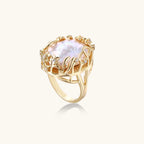 Gold filigree crown ring cradling an iridescent baroque freshwater pearl with crystal accents on white background