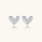 Pair of small heart-shaped stud earrings with brushed metallic finish, showing both silver and gold variants on neutral background.