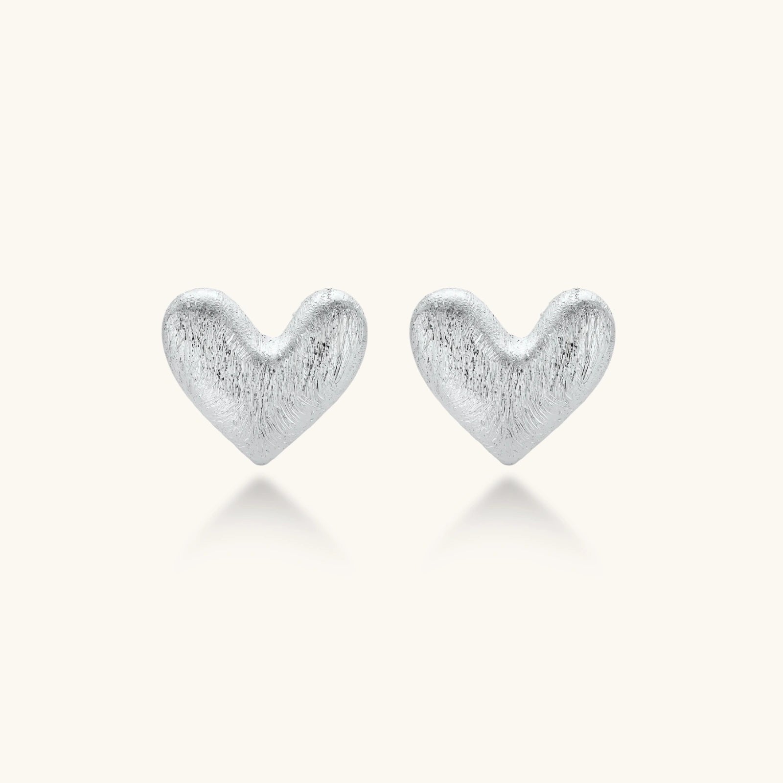 Pair of small heart-shaped stud earrings with brushed metallic finish, showing both silver and gold variants on neutral background.