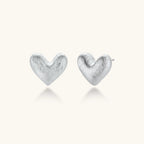 Pair of small heart-shaped stud earrings with brushed metallic finish, showing both silver and gold variants on neutral background.