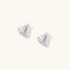 Pair of small heart-shaped stud earrings with brushed metallic finish, showing both silver and gold variants on neutral background.