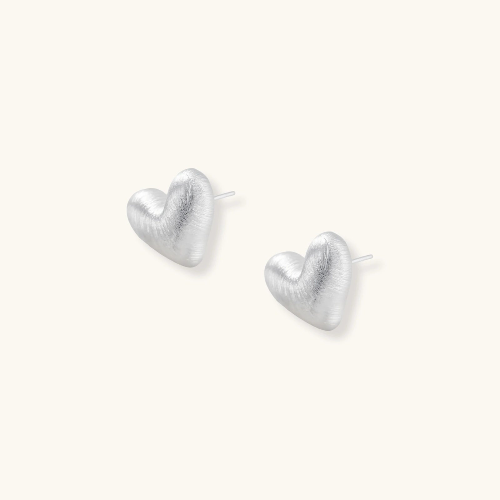 Pair of small heart-shaped stud earrings with brushed metallic finish, showing both silver and gold variants on neutral background.