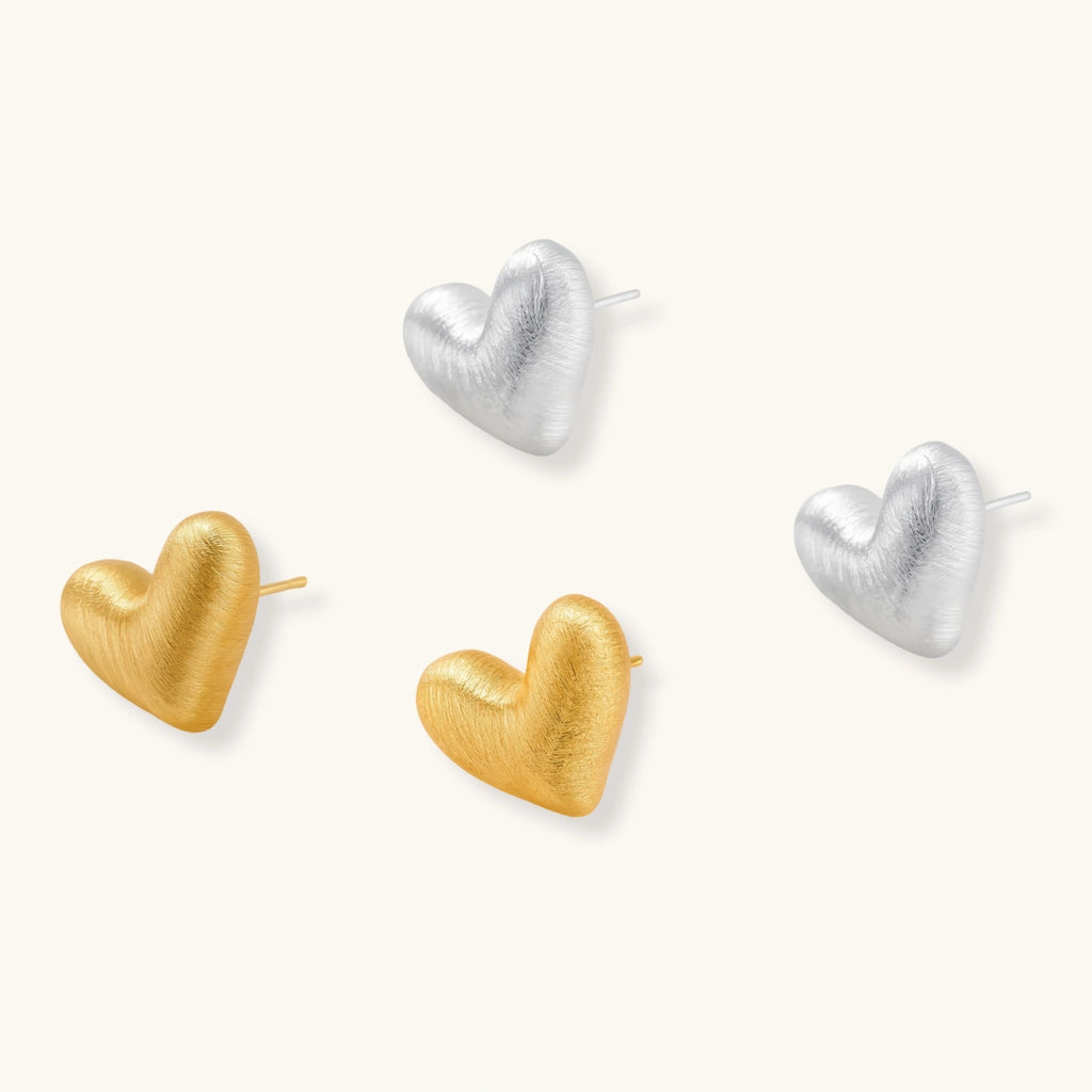 Pair of small heart-shaped stud earrings with brushed metallic finish, showing both silver and gold variants on neutral background.
