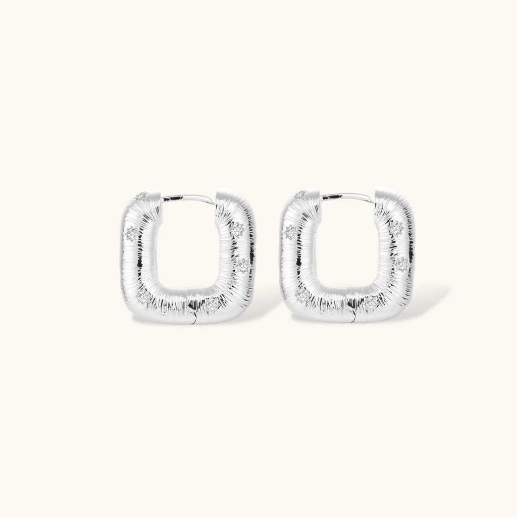 Close-up of ridged silver-plated hoop earrings with embedded crystal details on white background.