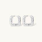 Close-up of ridged silver-plated hoop earrings with embedded crystal details on white background.