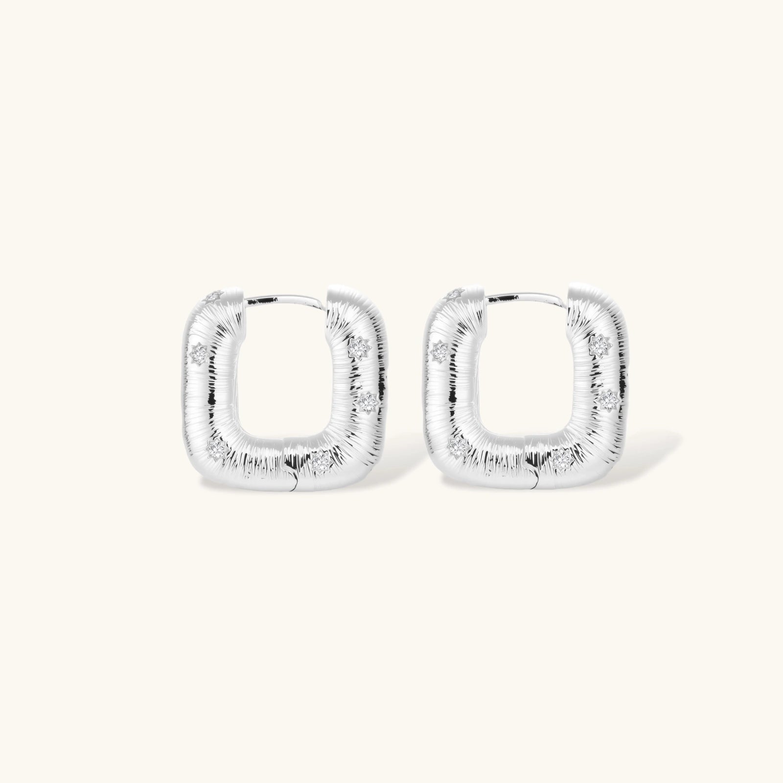 Close-up of ridged silver-plated hoop earrings with embedded crystal details on white background.
