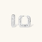 Close-up of ridged silver-plated hoop earrings with embedded crystal details on white background.