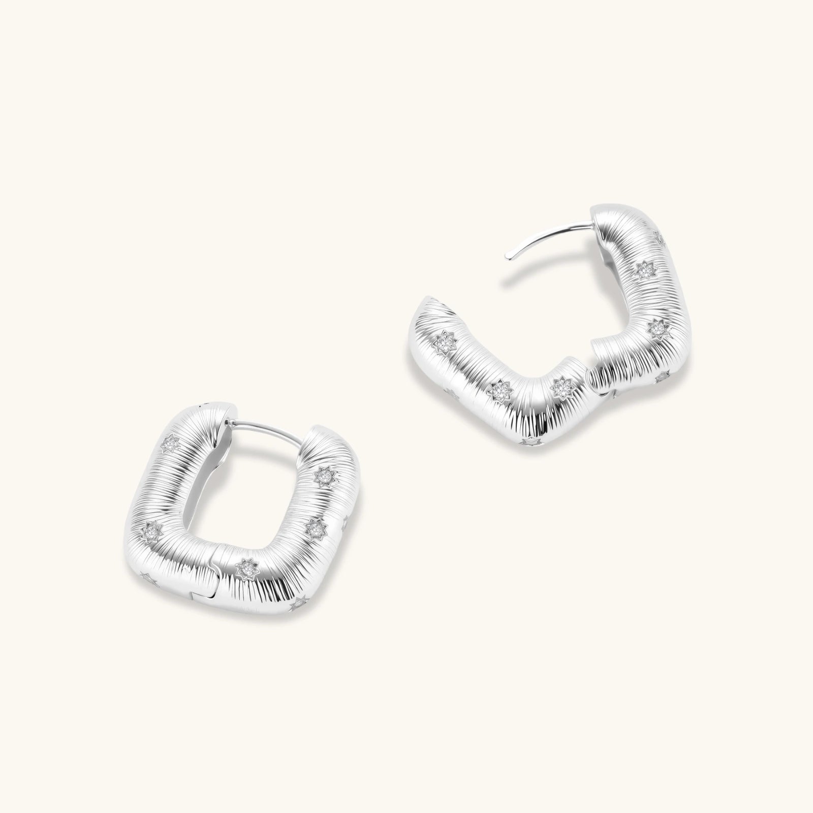 Close-up of ridged silver-plated hoop earrings with embedded crystal details on white background.